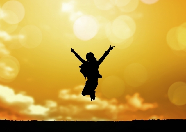 綺麗な夕焼けの中両手を広げ高くジャンプする女性