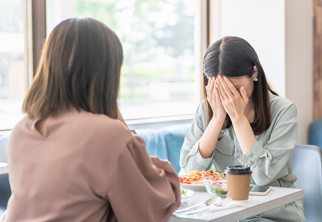 女性同士が喫茶店で話ながら片方の女性が涙を流している