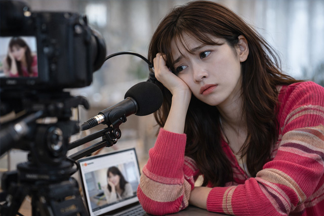 カメラとパソコンの前で頬杖をつき顔をしかめている女性